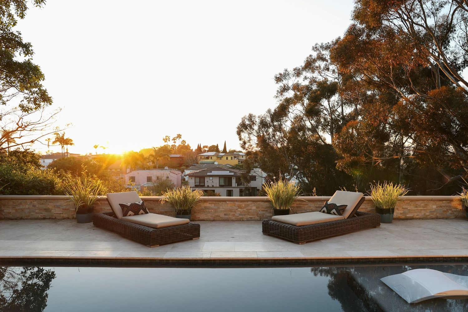 A stone pool terrace with two outdoor lounges at sunset, framed by gum trees